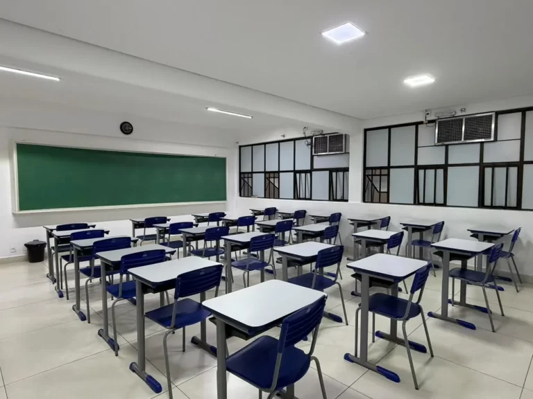 Sala de aula iluminada com lousa verde e carteiras individuais azuis enfileiradas
