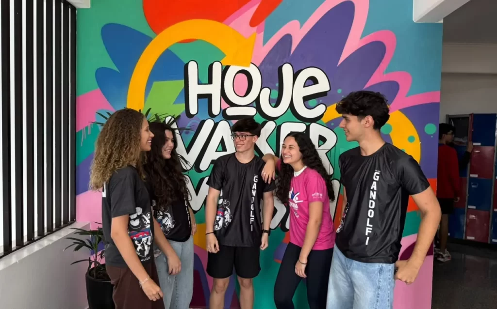 Grupo de alunos do Ensino Médio com camisetas do Gandolfi diante de um mural grafitado colorido