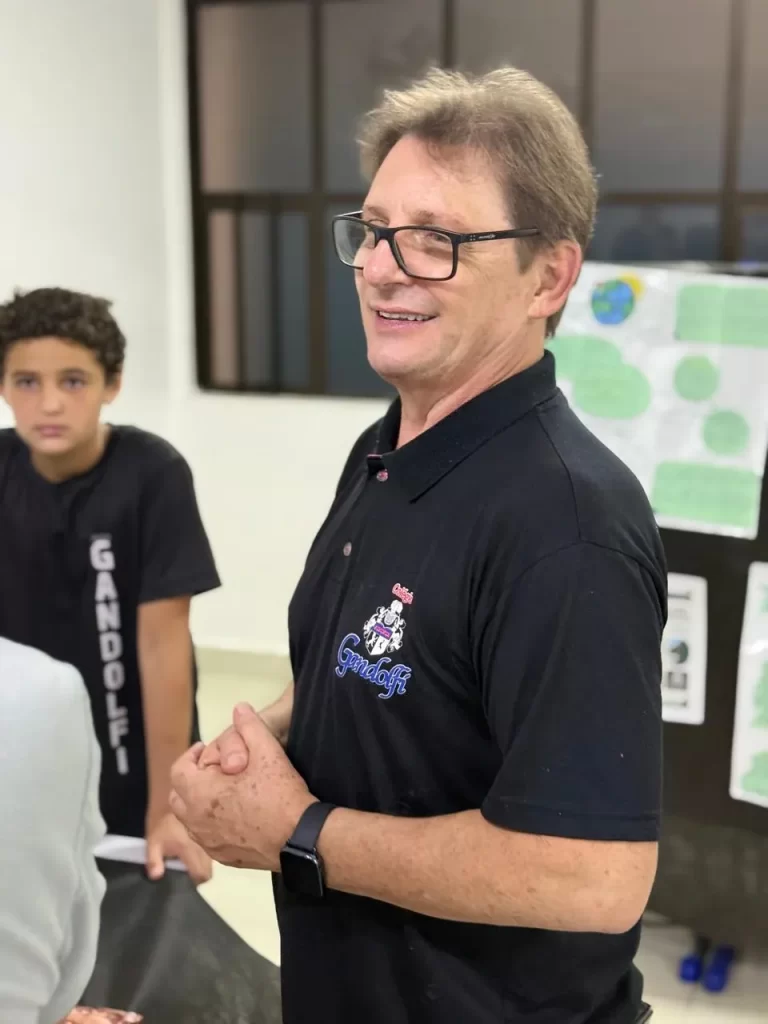 Professor com a camisa do Colégio Gandolfi conversando com alunos em sala de aula